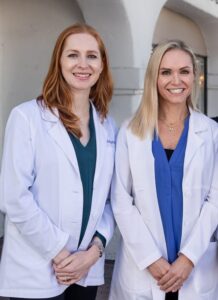 two women in white lab coats standing in front of a building