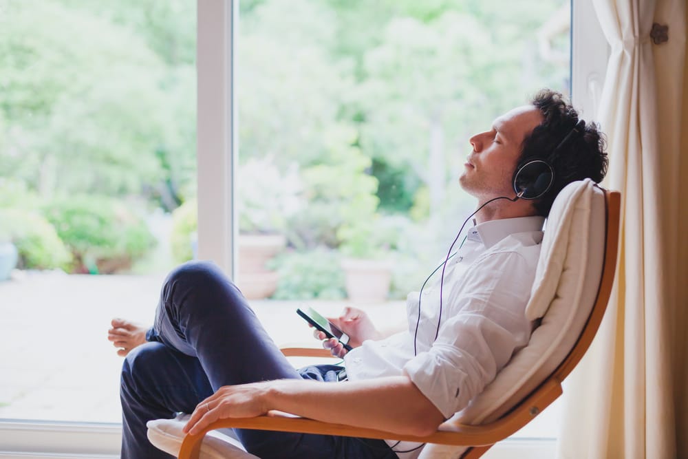 Relaxed man in headphones sitting in deck chair in modern bright interior