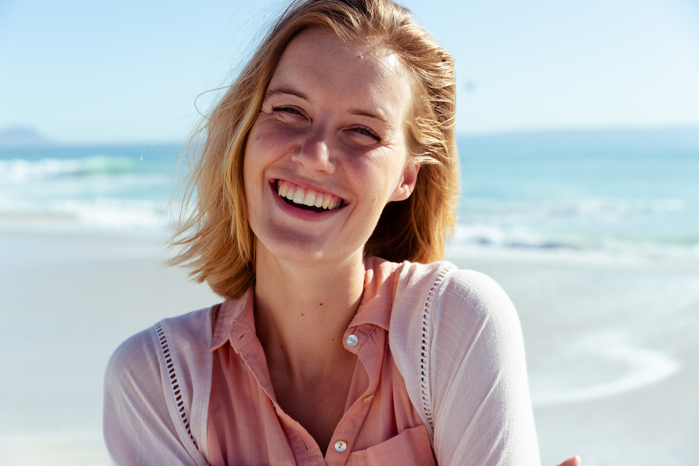 Portrait of a Caucasian woman enjoying time at the beach on a sunny day, looking at camera and smiling, with sea in the background