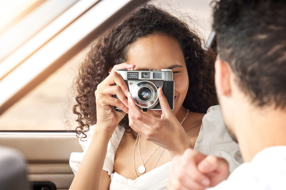 Shot of a young woman taking a picture of her boyfriend while sitting in a car together.
