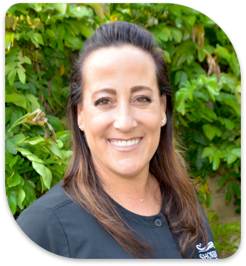 smiling woman with long brown hair and black shirt in front of bushes