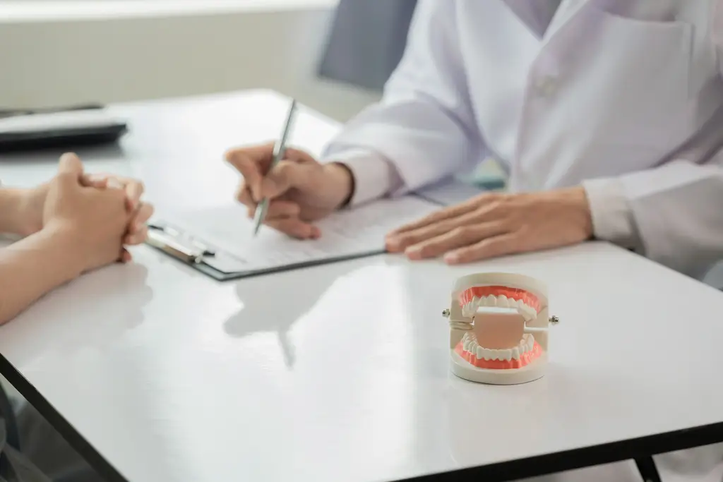 Dentist writing on a clipboard while consulting with a patient, with a dental model on the table.