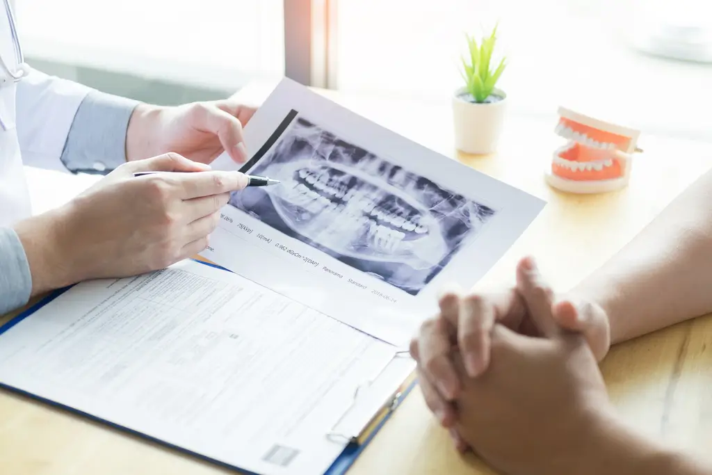 Dentist reviewing a dental X-ray with a patient, pointing at the image above a form on a clipboard.