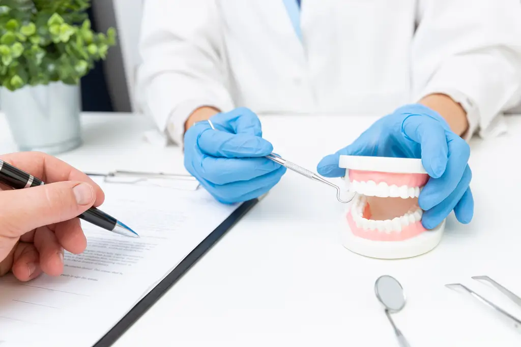 Dentist wearing blue gloves demonstrating dental tools on a teeth model during a consultation.