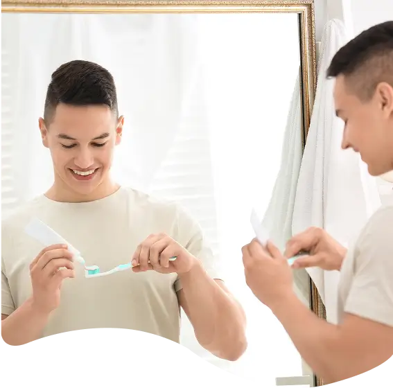 Teen boy brushing his teeth in front of a bathroom mirror, promoting teen dentistry and good hygiene habits.