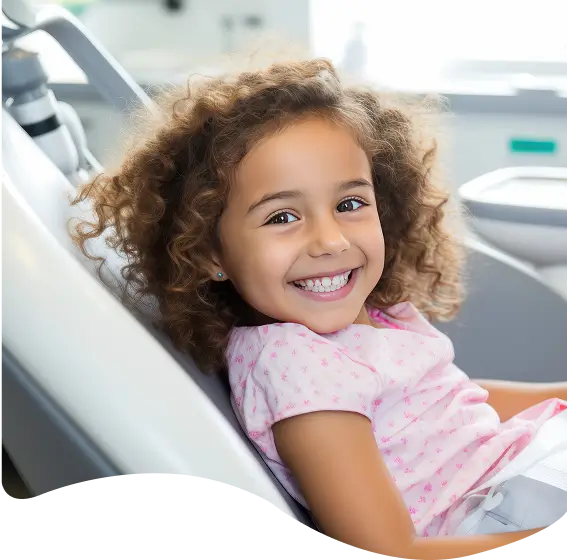 Young girl smiling while sitting in a dental chair, representing children’s dentistry services.