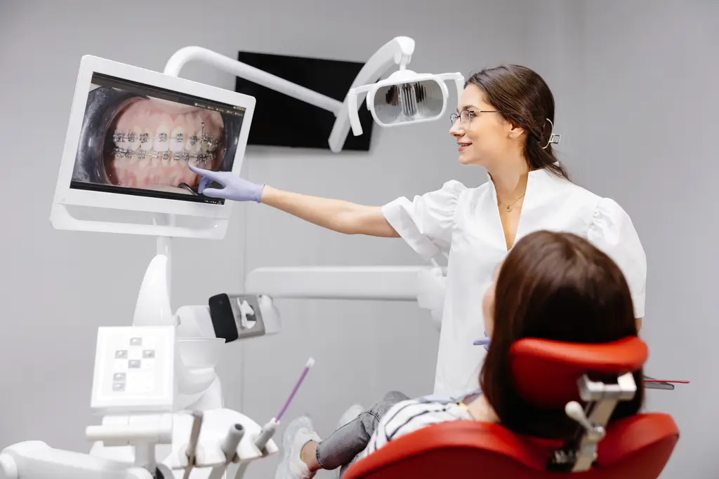 Dentist showing a patient digital images of teeth with braces on a monitor during an orthodontic consultation.